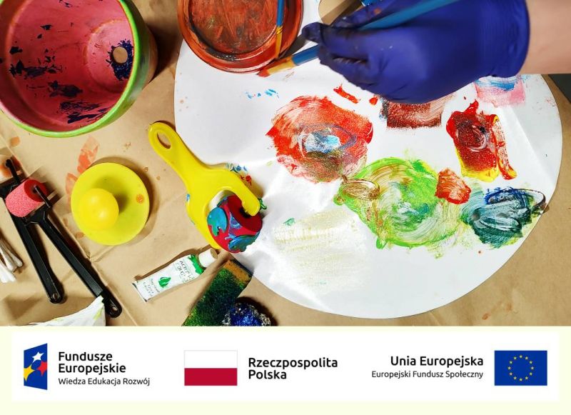 Grafika z logami: Funduszy Europejskich, RP, UE. Widoczna dłoń ozdabiająca naczynie. Na stole farby, przybory do malowania.