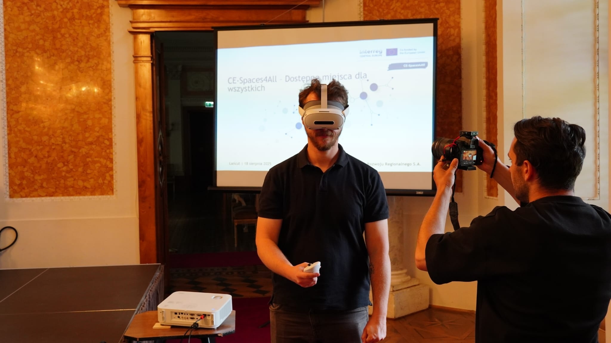 Sala Balowa, mężczyzna stoi, ma założone gogle VR, inny mężczyzna wykonuje mu zdjęcie